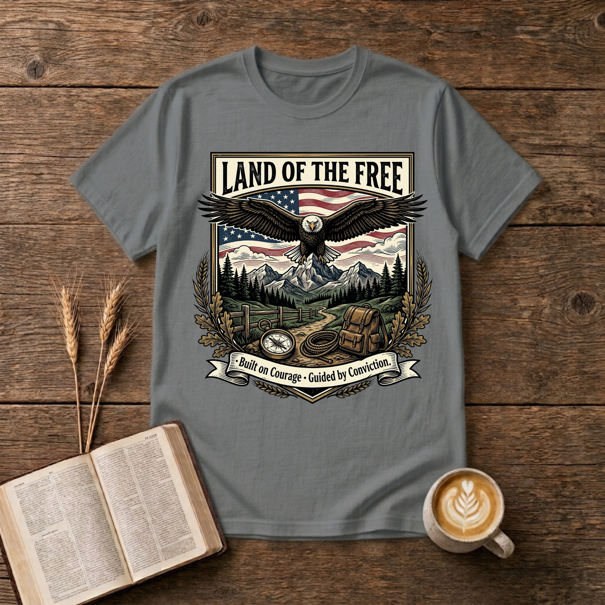 Monochrome eagle soaring above mountains and pines with a Land of the Free banner on a Graphite Heather unisex T-Shirt