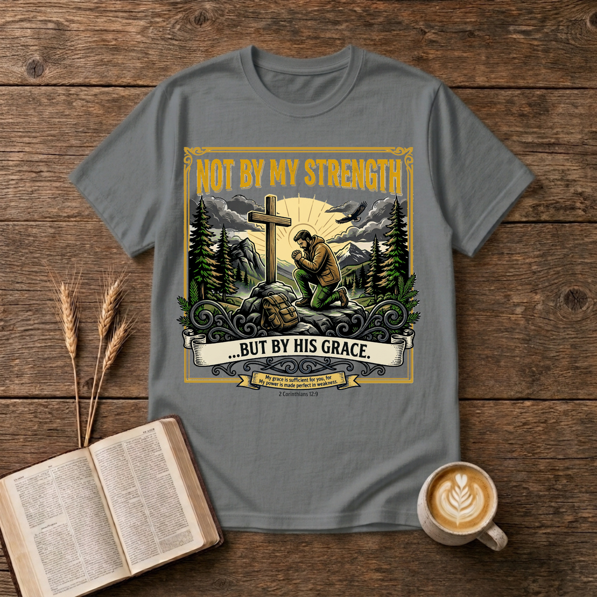 Figure kneeling at a cross in a forest clearing with Not By My Strength on a Graphite Heather unisex T-Shirt