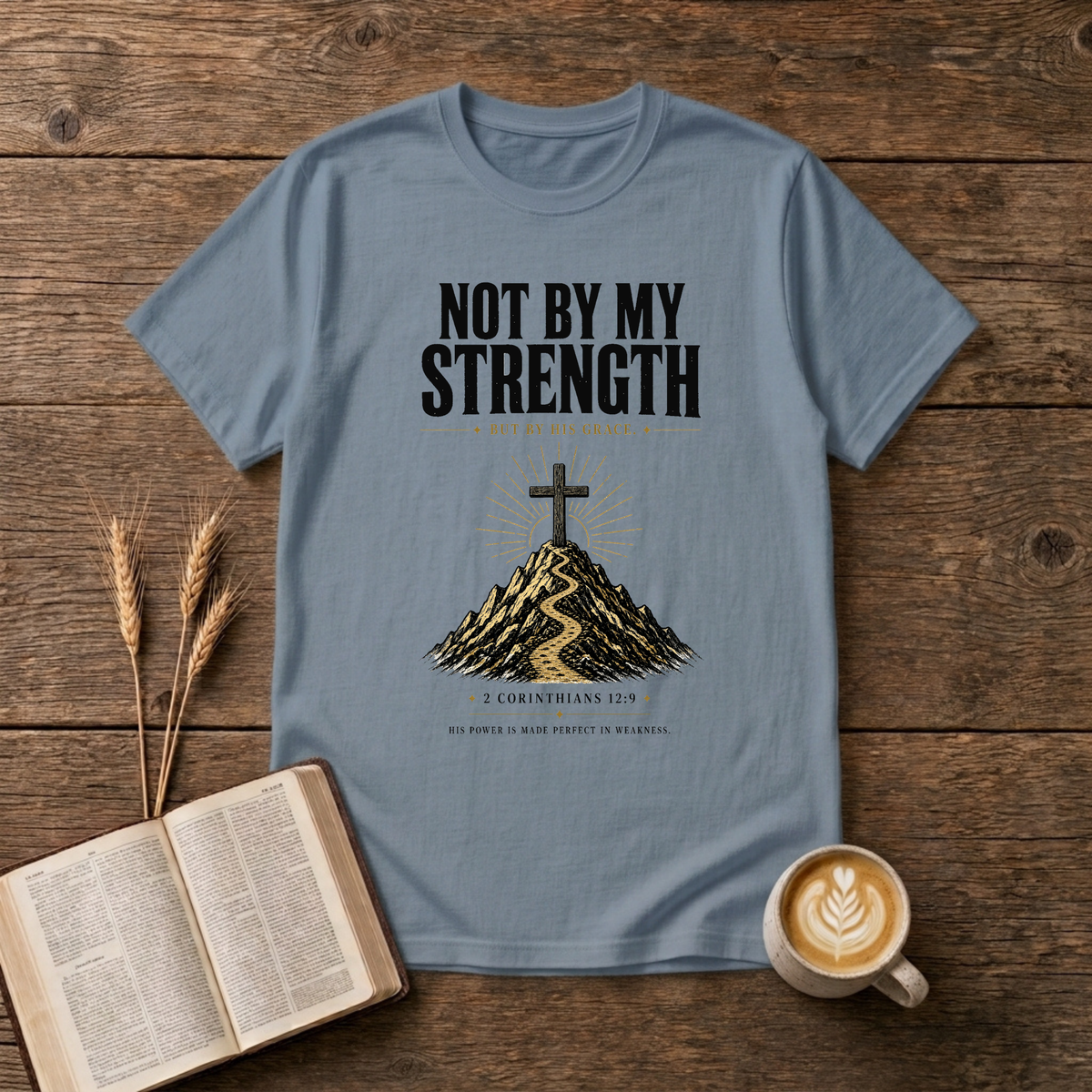 Distressed NOT BY MY STRENGTH lettering above a cross and mountain motif on a Stone Blue unisex T-Shirt