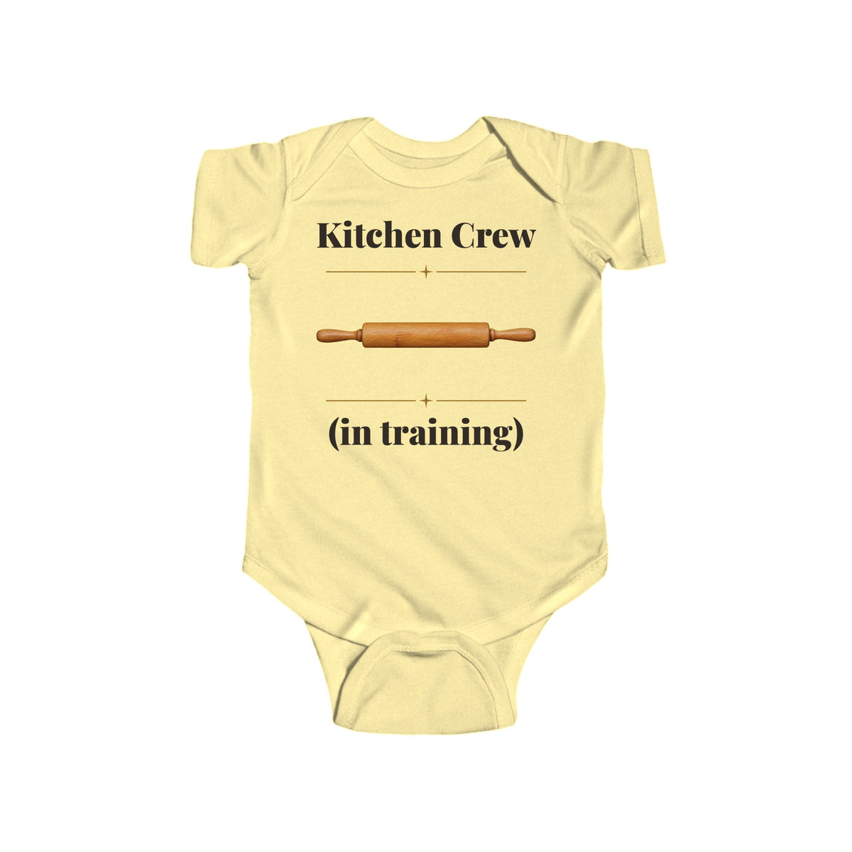 Kitchen Crew in Training baby bodysuit in Butter on a wood table with a knit blanket, wooden rattle and open Bible