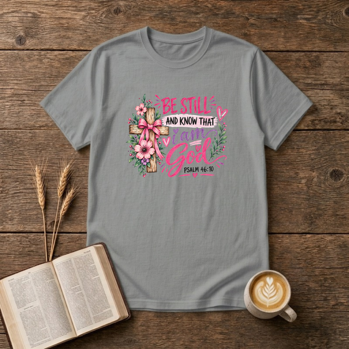 Be Still and Know That I Am God Psalm 46:10 design with a wooden cross wrapped in a pink bow and pink and purple flowers on a Sport Grey unisex T-Shirt