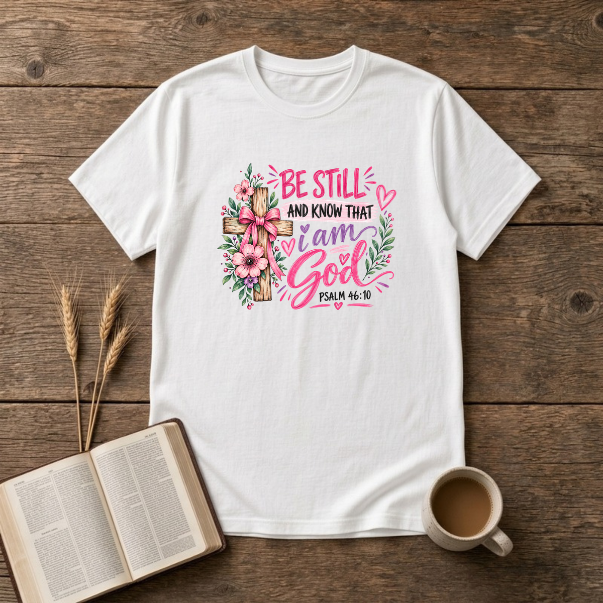 Be Still and Know That I Am God Psalm 46:10 design with a wooden cross wrapped in a pink bow and pink and purple flowers on a White unisex T-Shirt
