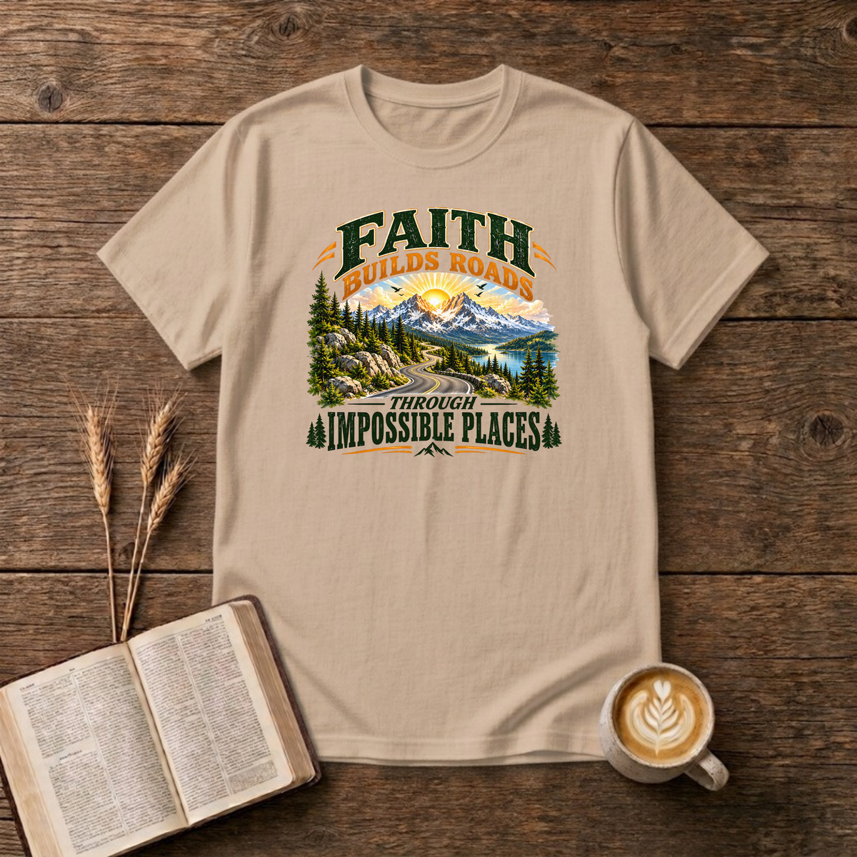 Faith Builds Roads Through Impossible Places design with dark green and orange lettering around a winding mountain road, evergreen forest, lake and sunrise on a Natural unisex T-Shirt