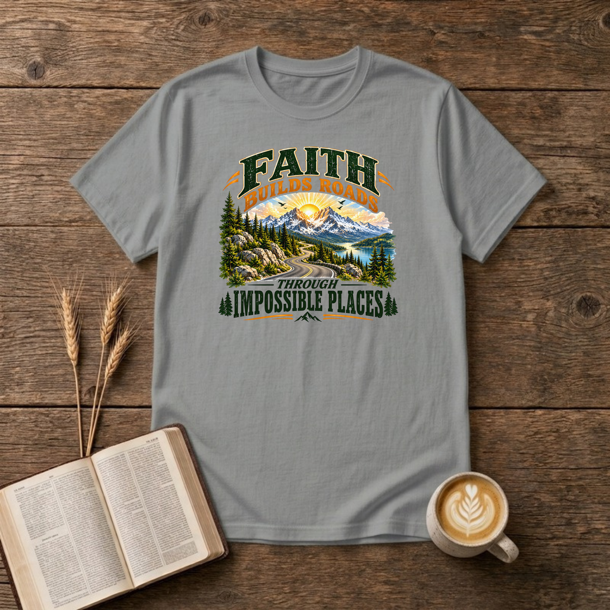 Faith Builds Roads Through Impossible Places design with dark green and orange lettering around a winding mountain road, evergreen forest, lake and sunrise on a Sport Grey unisex T-Shirt