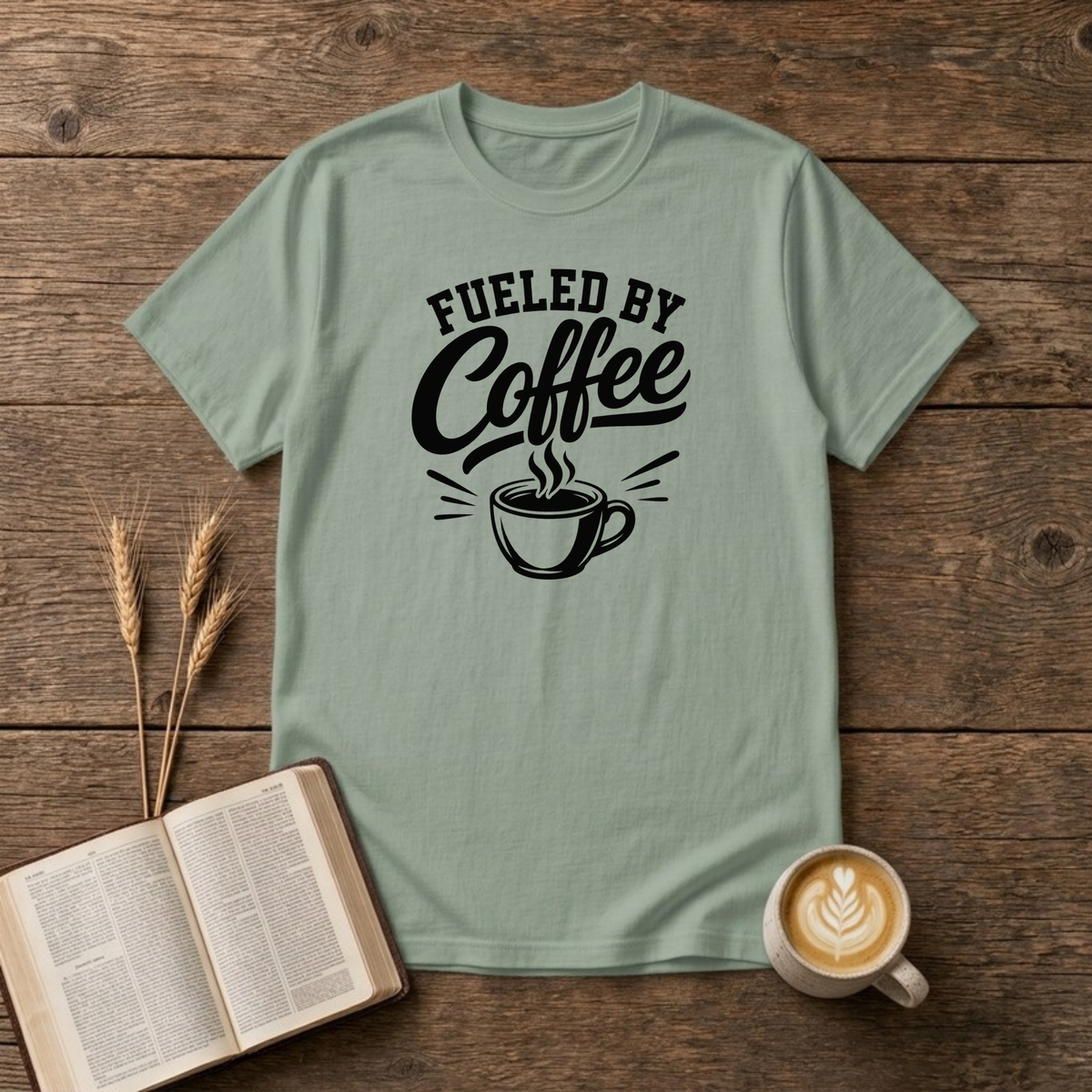 Fueled by Coffee design with black arched lettering above a steaming cup of coffee on a Sage unisex T-Shirt