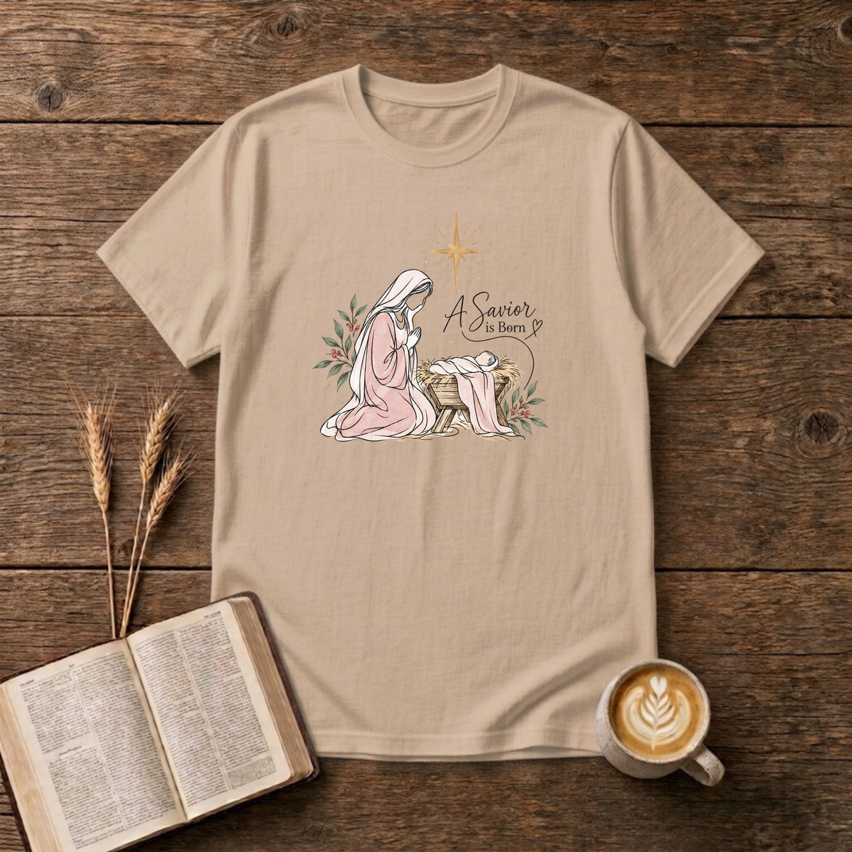 A Savior Is Born watercolor nativity design of Mary kneeling beside baby Jesus in the manger under a gold star on a Natural unisex T-Shirt