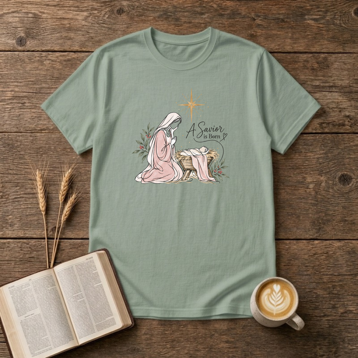 A Savior Is Born watercolor nativity design of Mary kneeling beside baby Jesus in the manger under a gold star on a Sage unisex T-Shirt