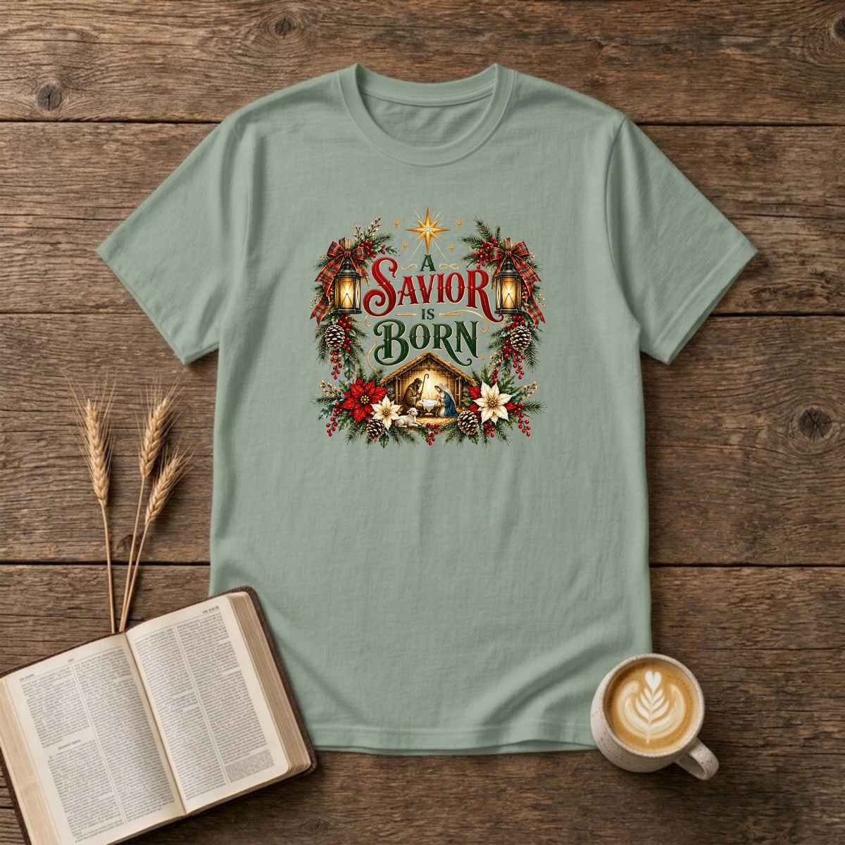 A Savior Is Born nativity wreath design with red and white poinsettias, holly and a lit stable scene on a Sage unisex T-Shirt