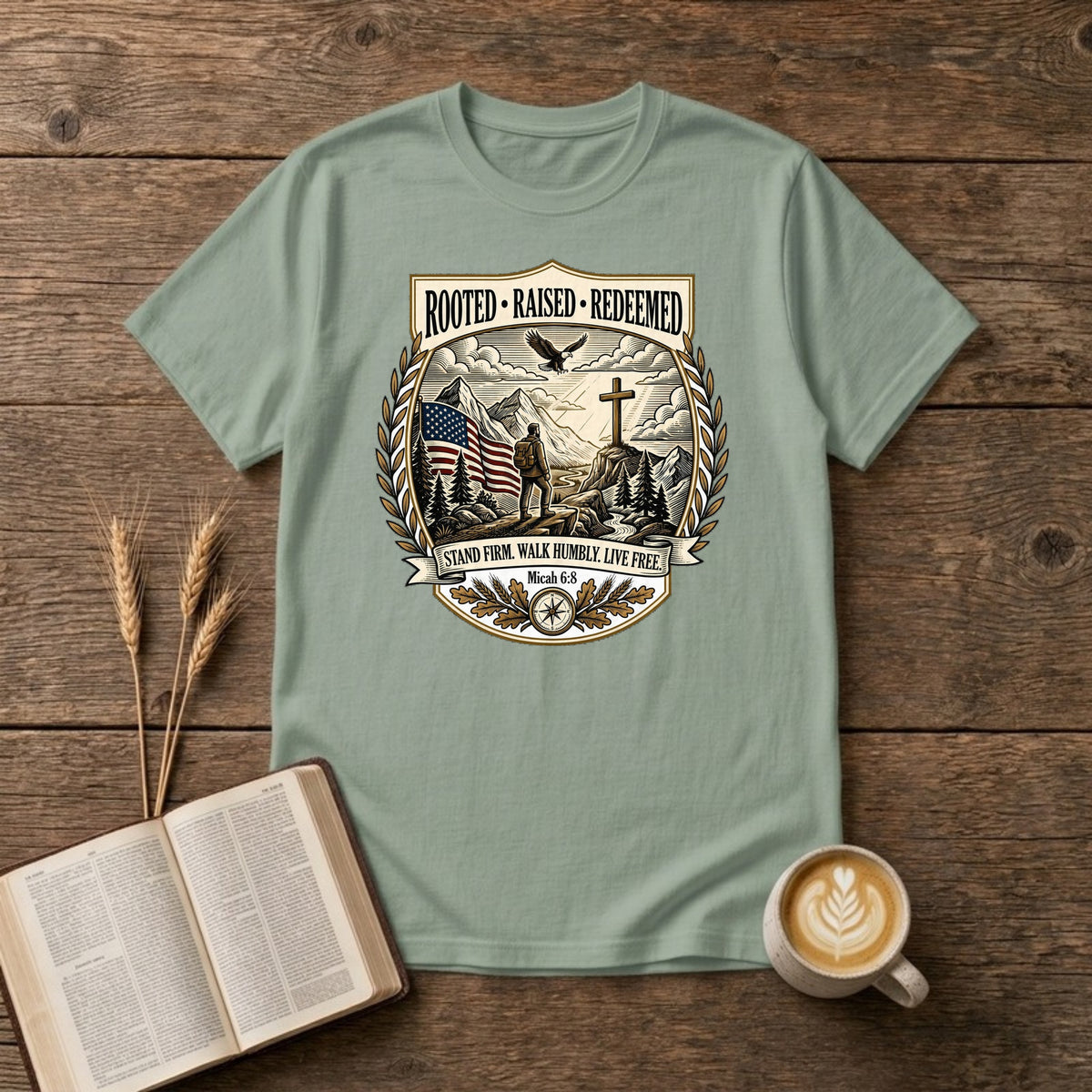 Rooted. Raised. Redeemed. crest badge with a hiker, cross, American flag, eagle and laurel frame on a Sage unisex T-shirt