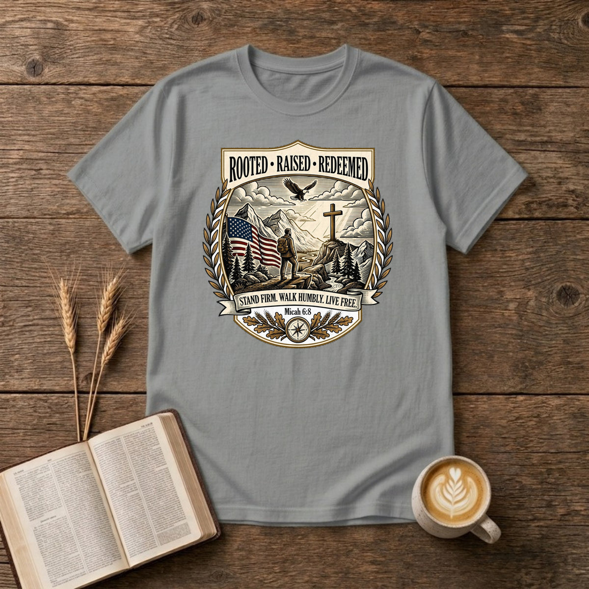 Rooted. Raised. Redeemed. crest badge with a hiker, cross, American flag, eagle and laurel frame on a Sport Grey unisex T-shirt