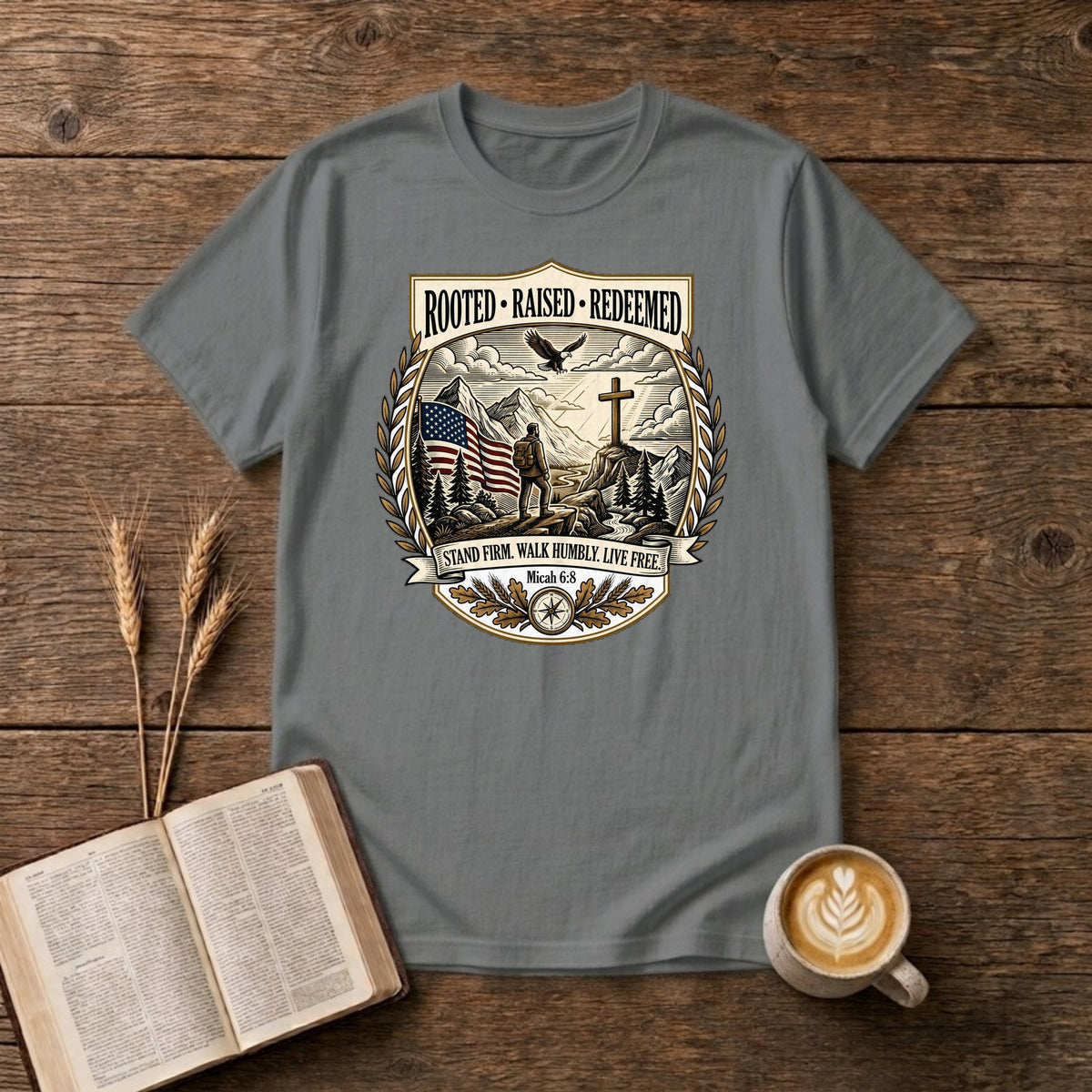 Rooted. Raised. Redeemed. crest badge with a hiker, cross, American flag, eagle and laurel frame on a Graphite Heather unisex T-shirt