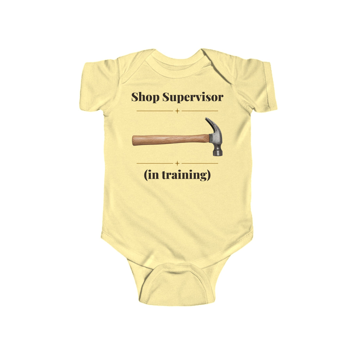 Shop Supervisor in Training baby bodysuit in Butter on a wood table with a knit blanket, wooden rattle and open Bible